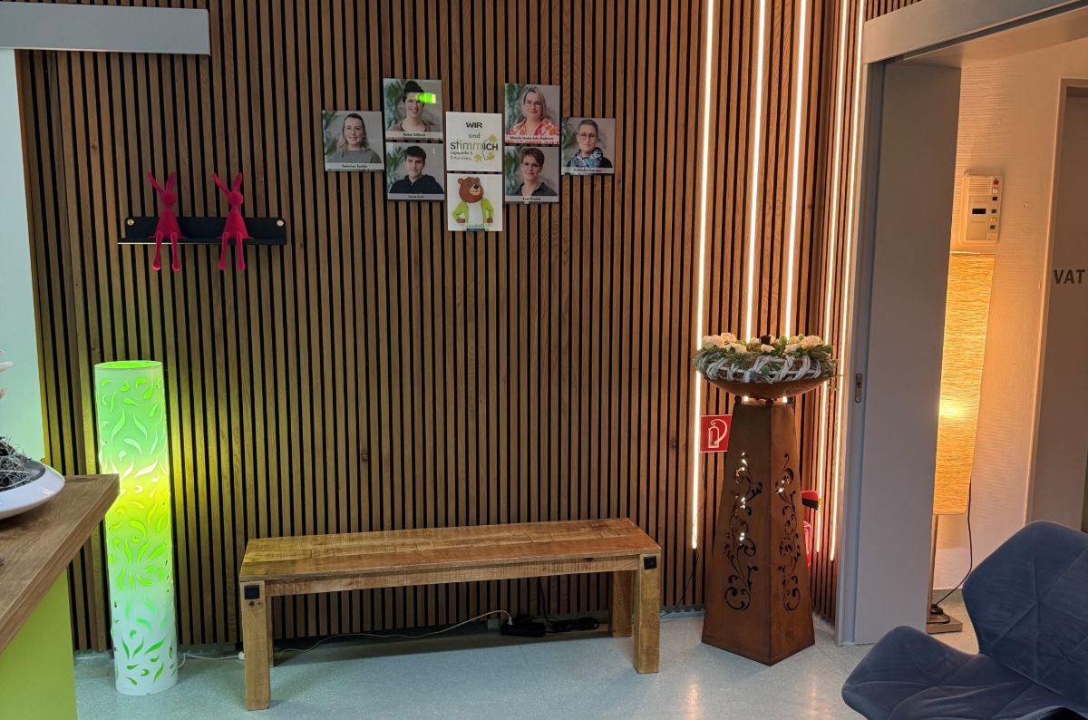 Wartebereich mit holzvertäfelter Wand, Teambildern und einer Holzbank.