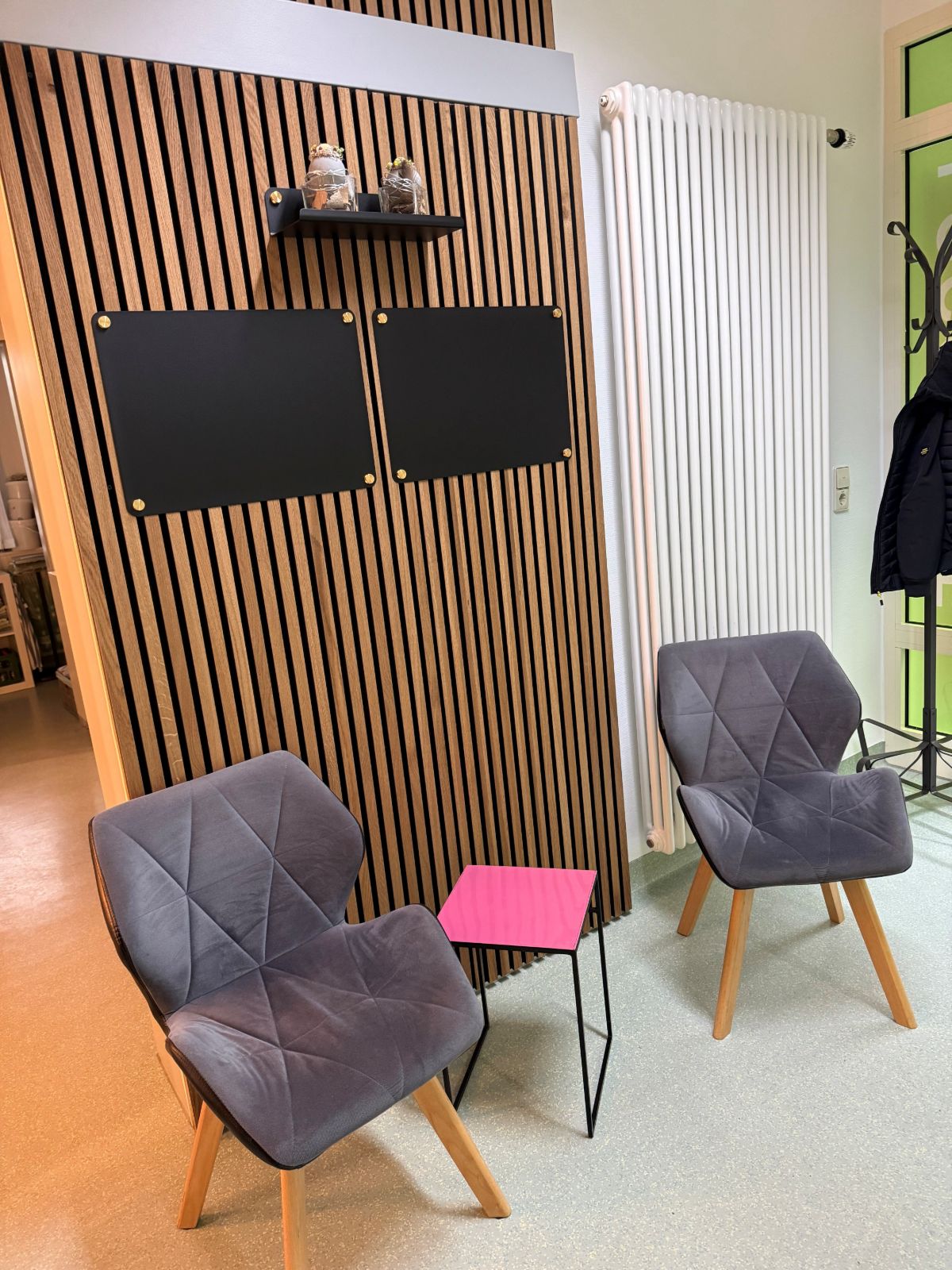 Wartebereich mit holzvertäfelter Wand und zwei Polsterstühlen.