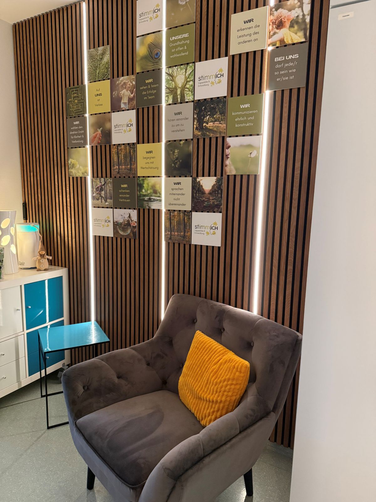 Wartebereich einer Praxis mit holzvertäfelter Wand und kleinen Bildern, davor ein Sessel.