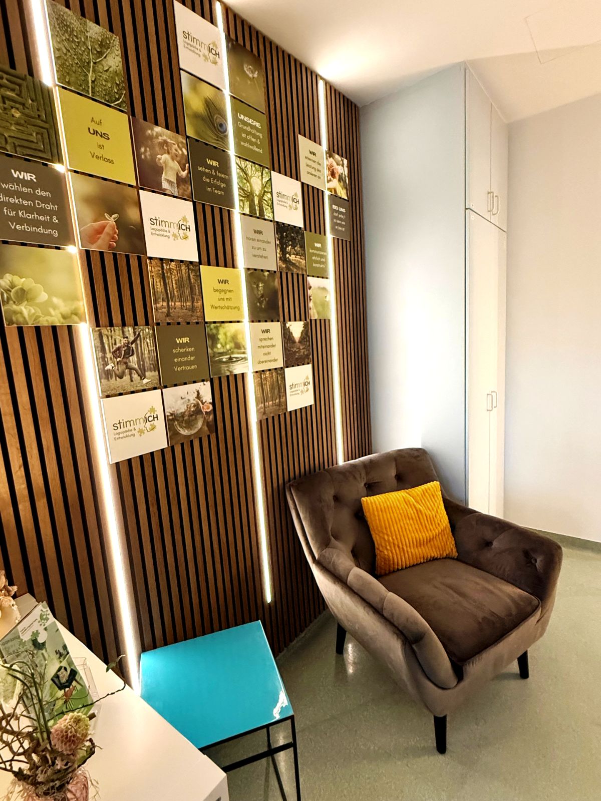 Wartebereich mit gemütlichem Sessel, holzvertäfelter Wand und vielen kleinen Bildern.