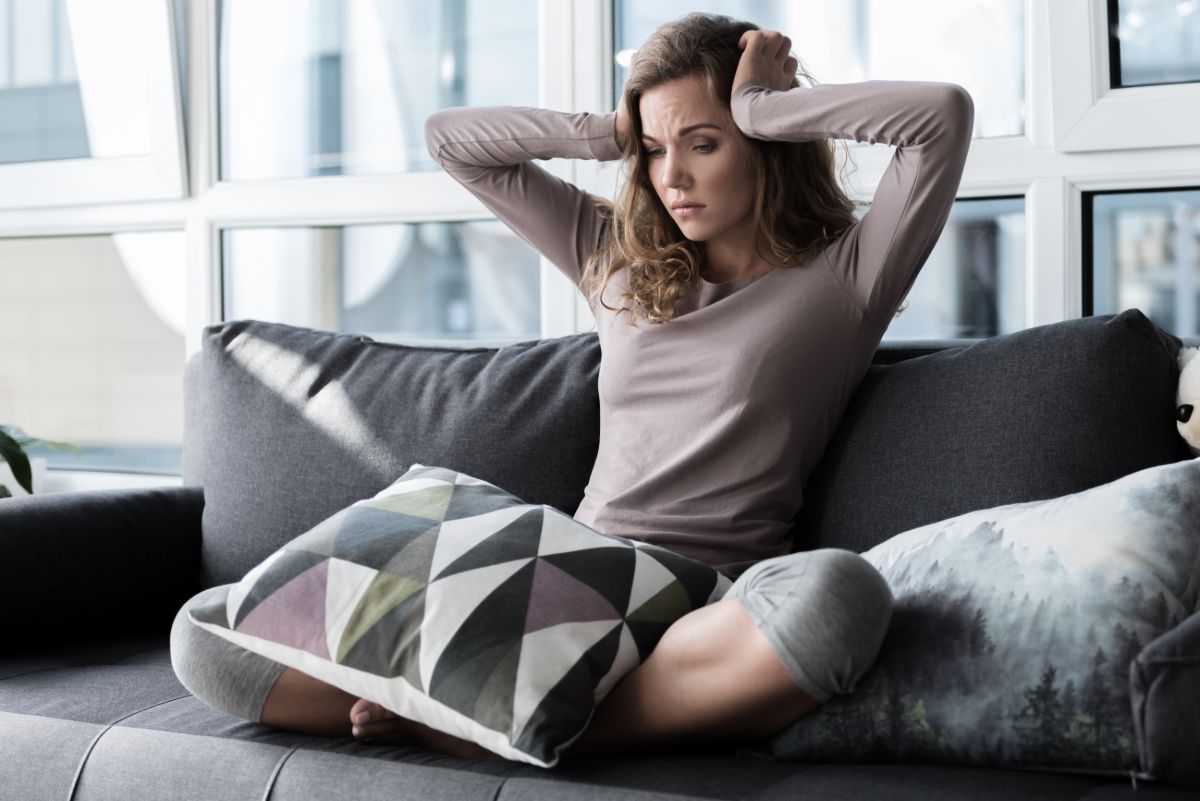 Frau sitzt auf Sofa und hält sich den Kopf
