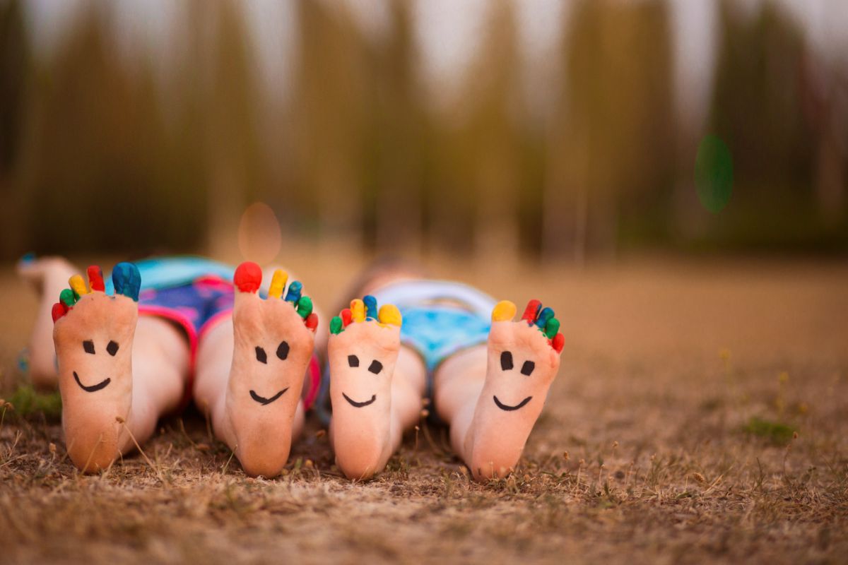 Zwei Paar Kinderfüße mit bunt angemalten Zehen und aufgemalten lachenden Gesichtern.