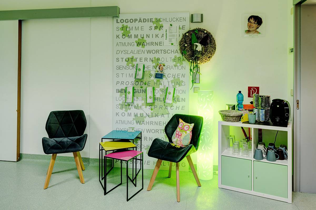 Wartebereich mit schwarzen Stühlen, buntem Tisch und Schrank.