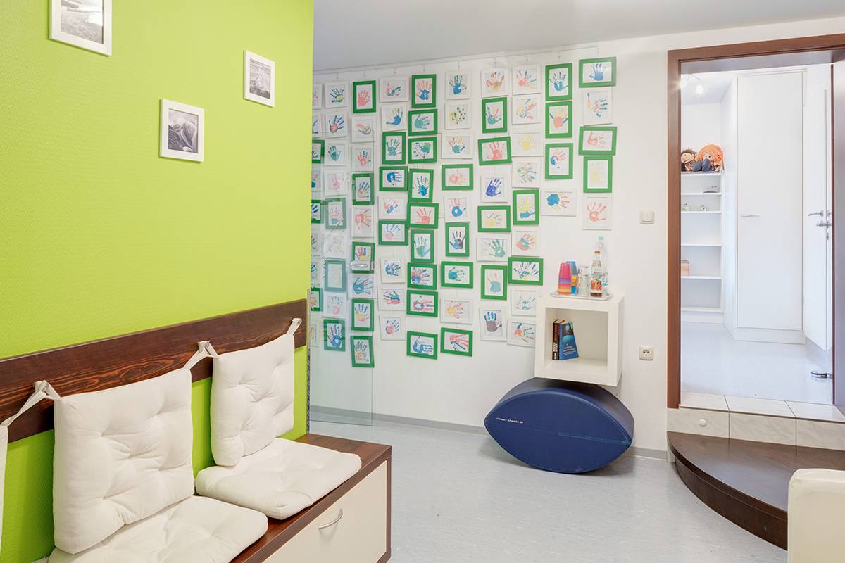 Wartebereich mit grüner Wand und Handabdruckbildern.