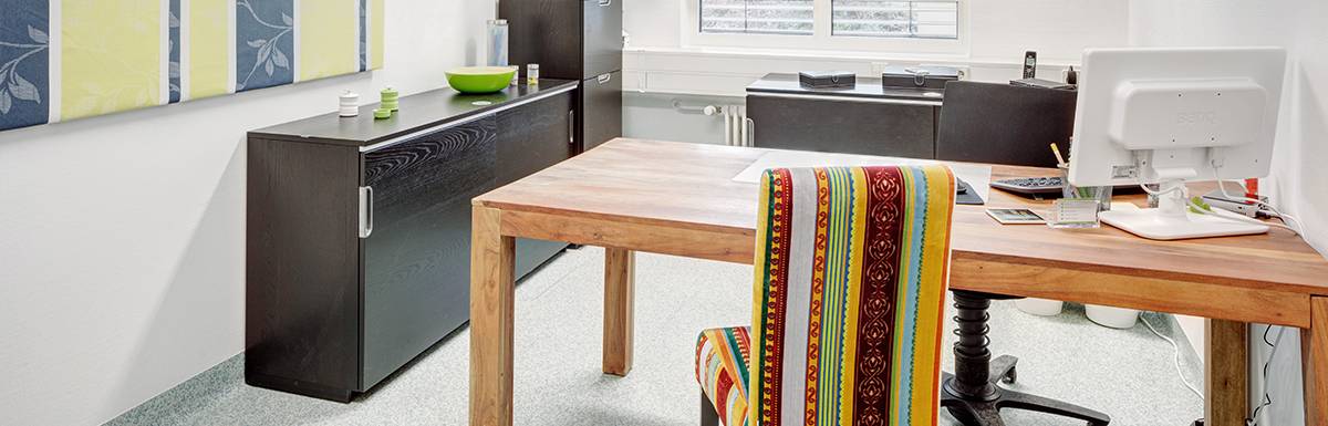 Raum mit Holzschreibtisch und bunter Stuhlhülle.