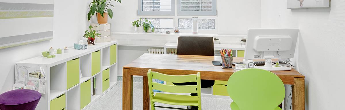 Büro mit Holzschreibtisch und grünen Stühlen.