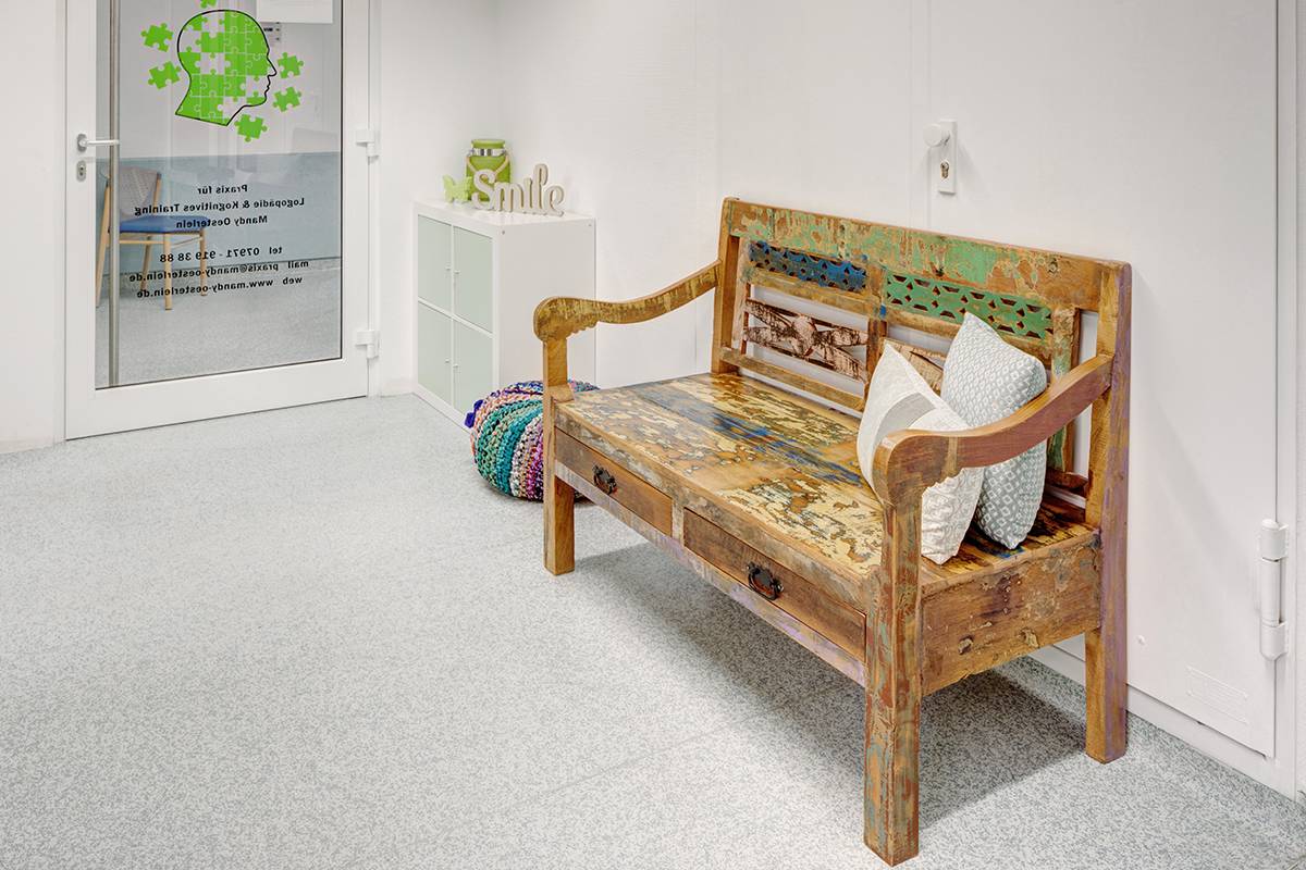 Wartebereich mit antiker Holzbank und Kissen.