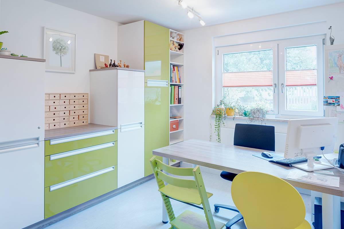 Buntes Büro mit Schreibtisch und grünen Stühlen.